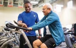 Seniors - A personal trainer offers instruction to a YMCA member on a cycle bike in the wellness center. 