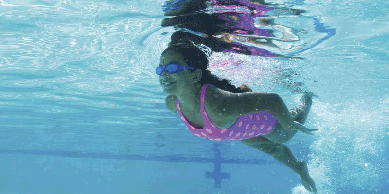 A girl in a pink bathing suit swims in the outdoor swimming pool