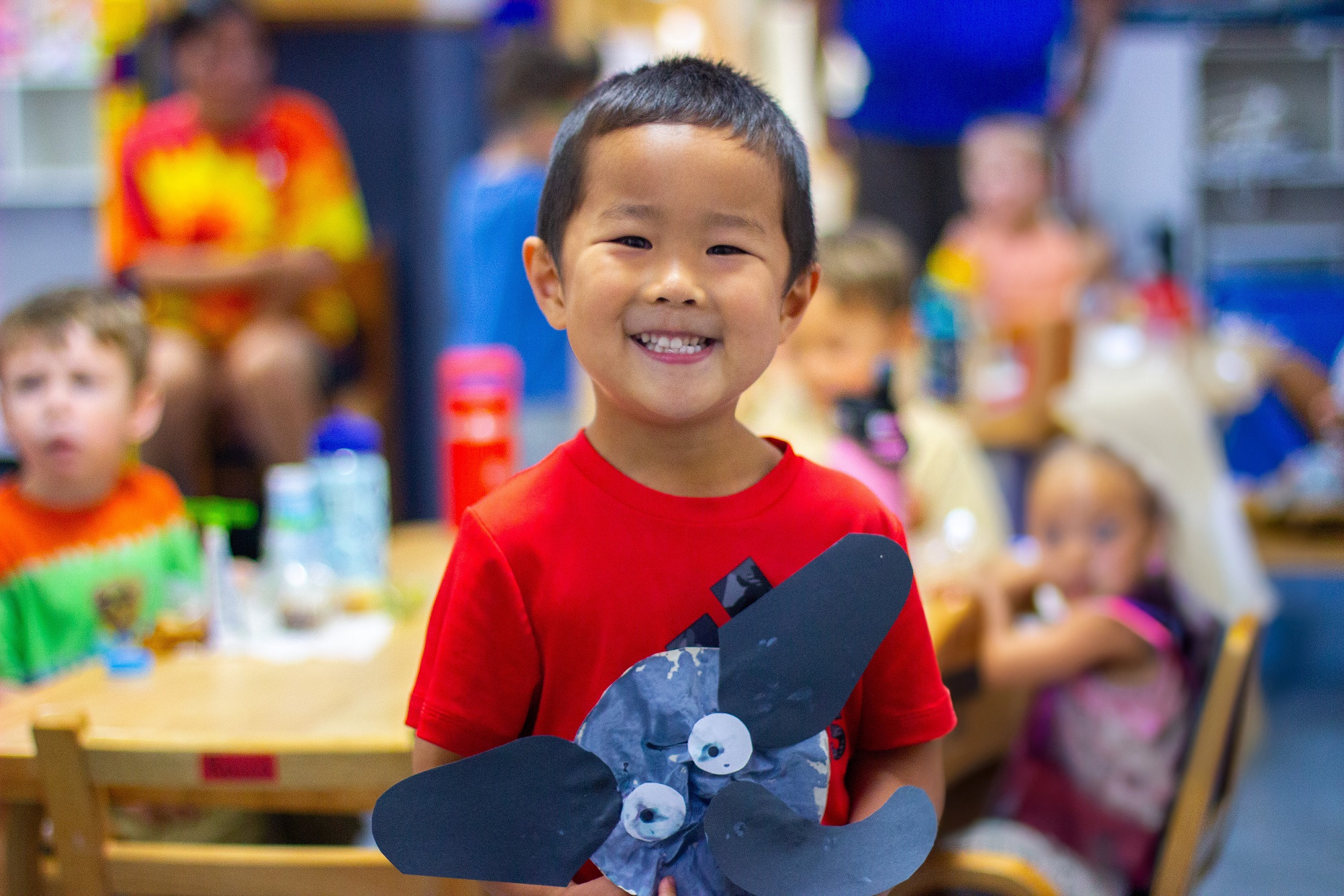 A student in an early learning classroom proudly showcases an art project.
