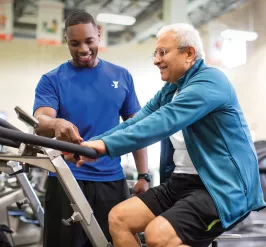 Seniors - A personal trainer offers instruction to a YMCA member on a cycle bike in the wellness center. 
