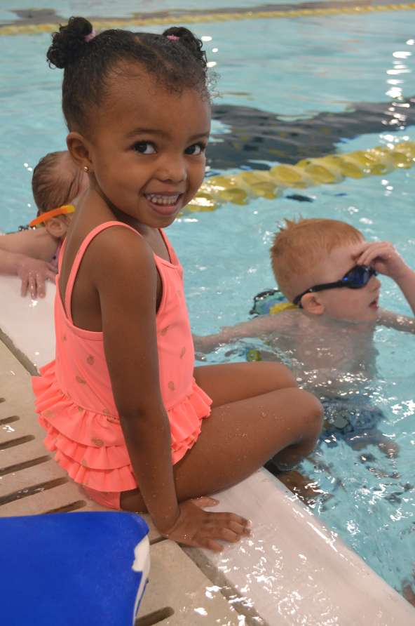 A preschool student sits on the side of the indoor swimming pool while learning to swim during a YMCA swim lesson.