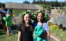 Two teenage girls at the Environmental Education program at Upper Main Line pose with lettuce on their heads.