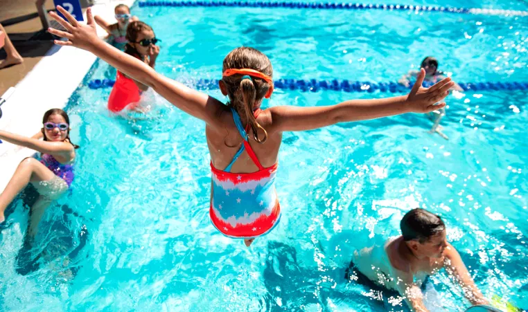 A girl attending summer camp at the West Chester Area YMCA jumps into the outdoor swimming pool during swim time.