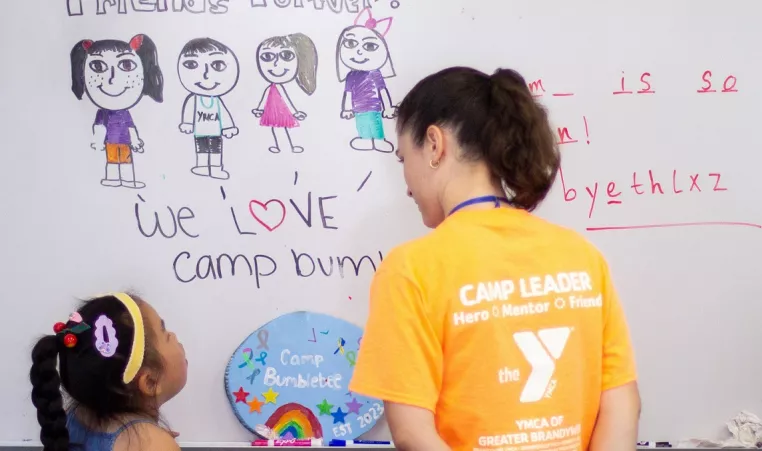 A YGBW camp counselor draws on a whiteboard with a camper at BumbleBee Day Camp at the Upper Main Line Branch in Berwyn during the summer of 2023.