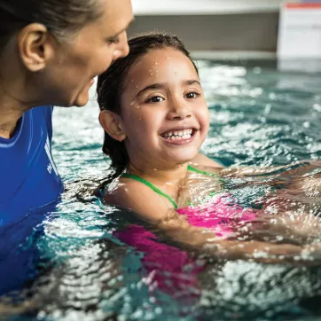 A girl smiles in the pool while learning to swim during a YMCA swimming lesson.